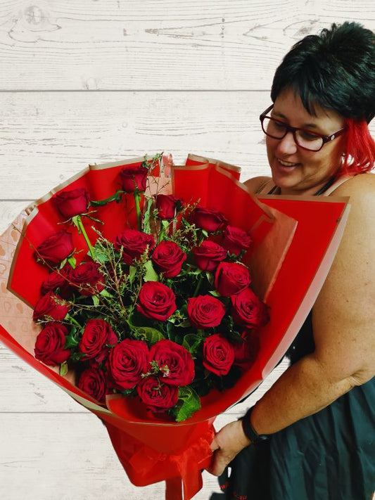 a lady holding a bouquet of 24 red roses with foliage wrapped in red and pink paper.