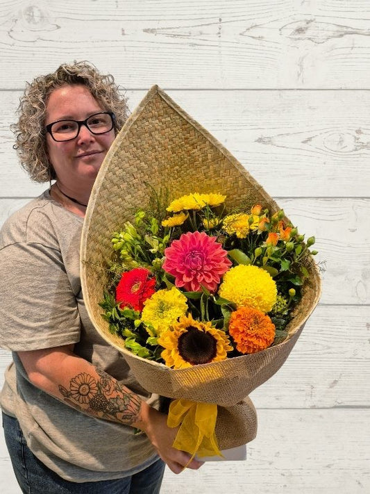 bright bouquet of flowers in a harakeke flax wrap with yellow bow