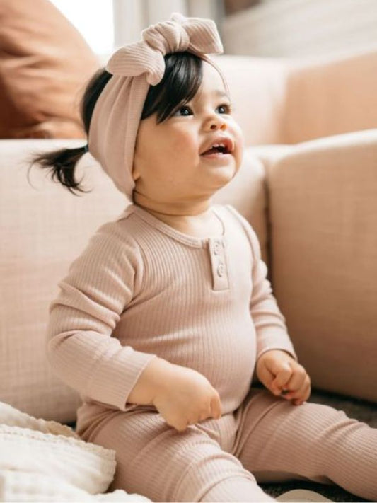 A long sleeve beige bodysuit for babies, presented on a wooden background.