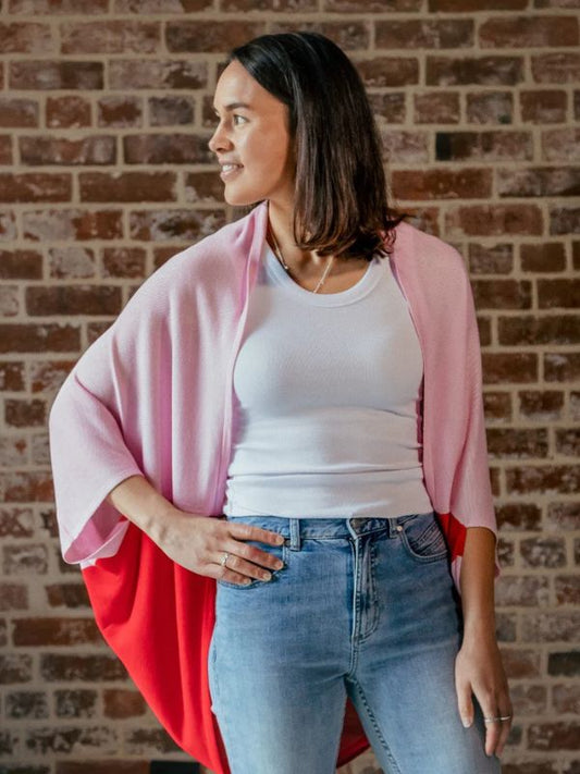 A person standing in front of a brick wall, wearing a red cardigan over a white top and blue jeans.