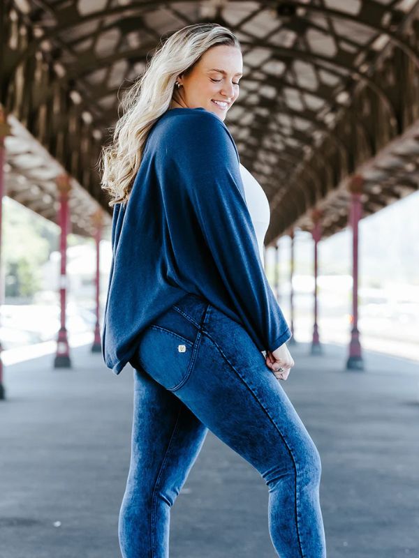 A woman is wearing a navy cardigan with kimono style sleeves over a white top, paired with blue jeans.