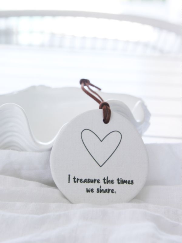 A white ceramic plaque with an embossed heart and the text 'I treasure the times we share', displayed on a white surface with a rope for hanging.