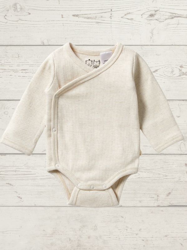 A beige long sleeve rib kimono bodysuit for babies, with a cross-over neckline and snap opening, displayed on a wooden background.