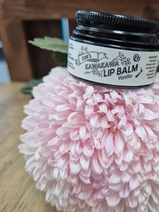 a black pottle with a white label on it with the words Lip Balm, on a pink chrysanthemum on a wooden surface