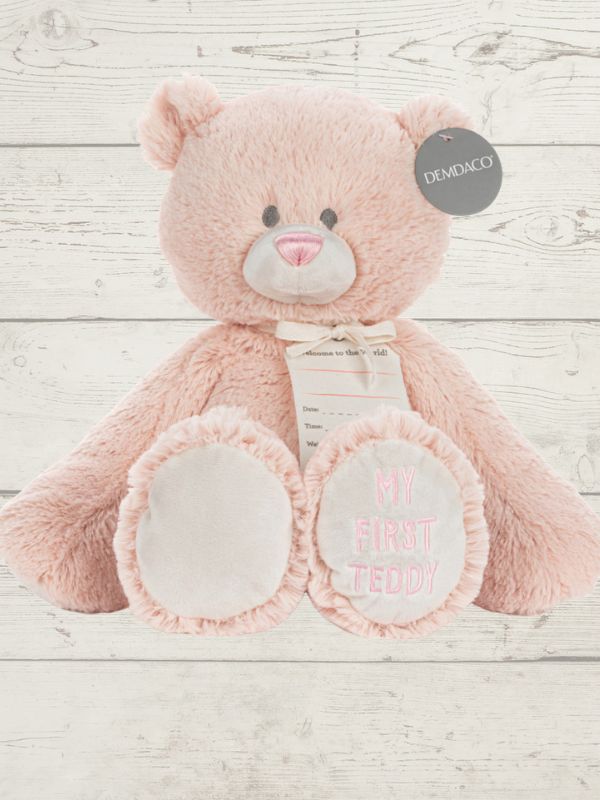 Pink teddy bear with 'My First Teddy' text on a wooden surface