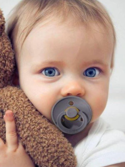 A baby holding a BIBS pacifier with an anatomical nipple design.
