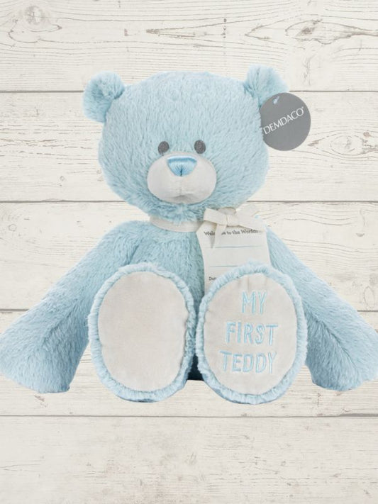 Blue teddy bear with 'My First Teddy' text on a wooden surface