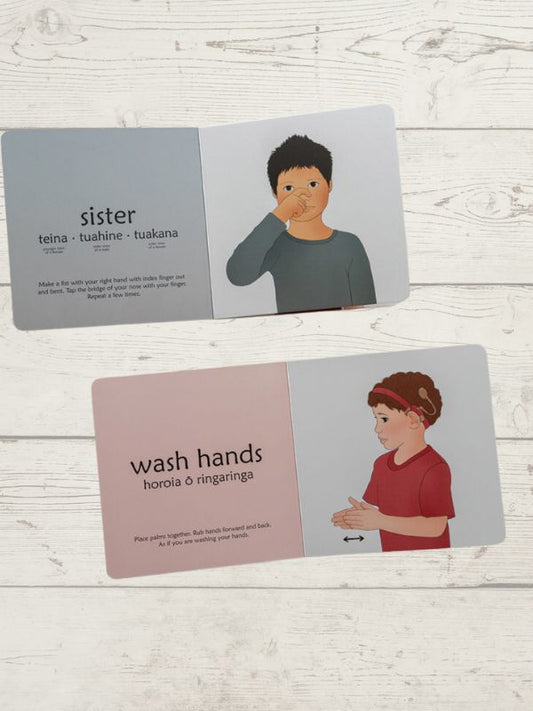 book showing children using sign language, with the words "sister" and "wash hands" on a wooden surface