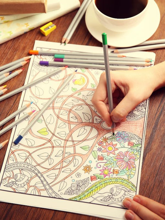 coffee cup, coloured pencils and colouring book with a tree and flowers