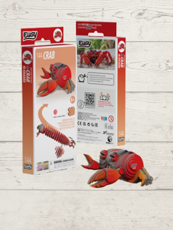 A 3D wooden puzzle kit of a crab, shown with its retail packaging boxes and the assembled puzzle piece layout on a light wood background. The brand 'EWLSY' is visible on the packaging.