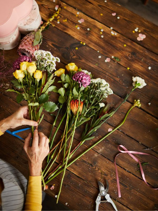 A person is arranging a bouquet of various flowers on a wooden table, including roses and other flowers.