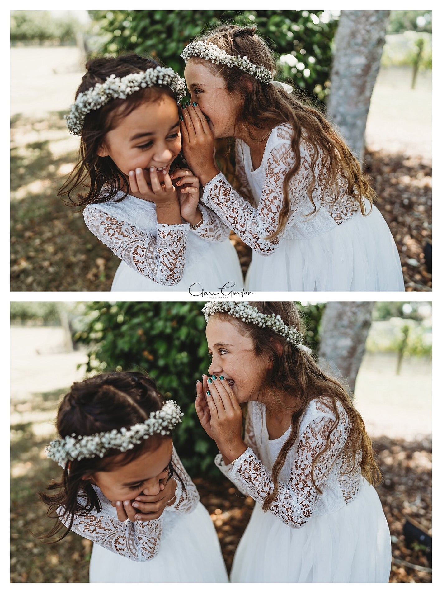 Two young girls in white dresses with lace details and flower crowns, one whispering to the other outdoors.
