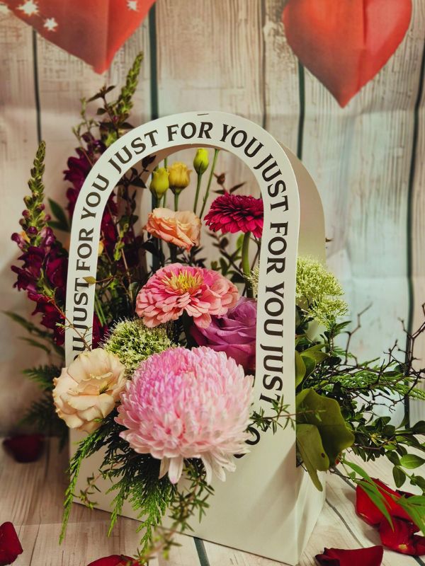 flowers in pinks and reds displayed in container with handle. Handle has the words just for you on it.