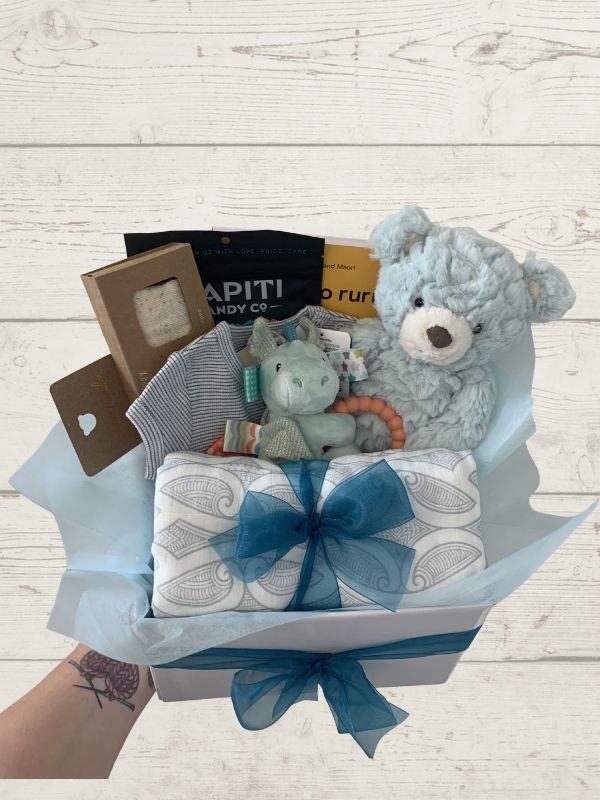 Gift basket with baby items including teddy bears and a blanket on a wooden surface.