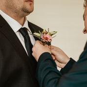 Person adjusting a boutonniere on another person's suit jacket.