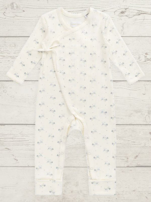 An off-white long-sleeve baby romper with a tiny blue and gray floral pattern, laid flat on a light gray wood plank background.