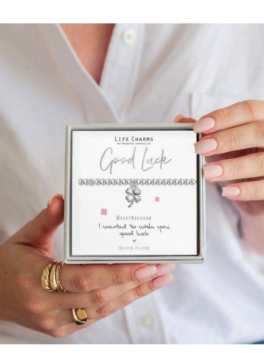 Person holding a box of Life Charms with a bracelet labeled 'Good Luck'.