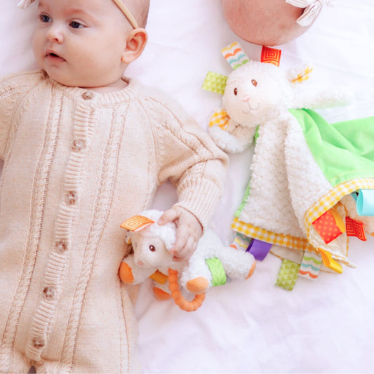 Baby holding a colorful lamb rattle with another toy in the background