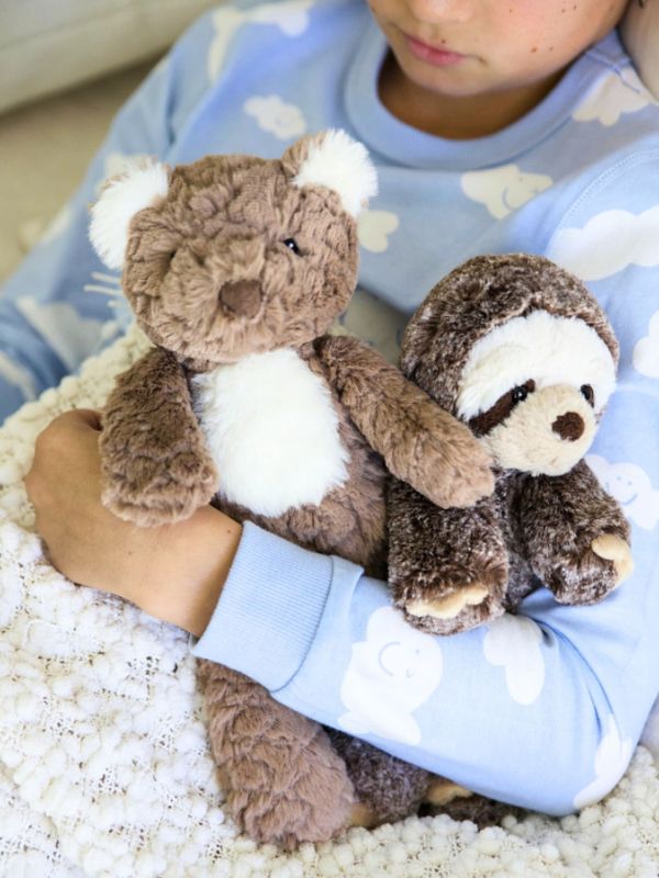 Child holding two teddy bears against a light blue blanket with white cloud patterns.