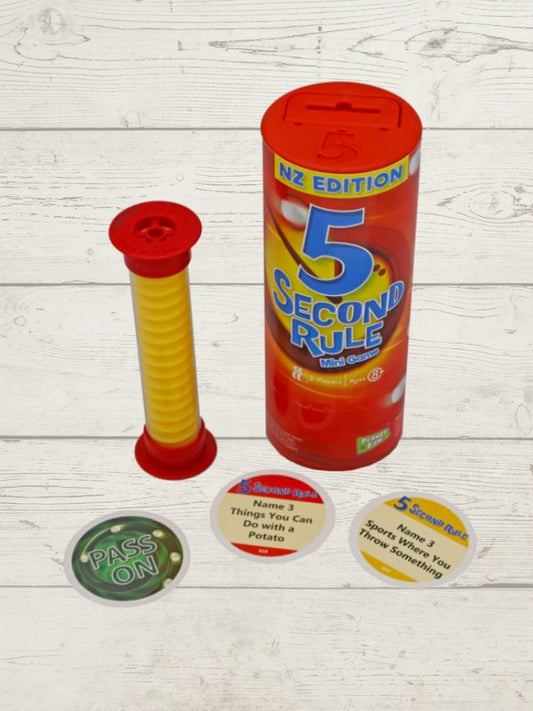 A mini version of the 5 Second Rule game displayed with a red cylindrical timer, yellow spiral timer, and several question cards laid out on a wooden surface.
