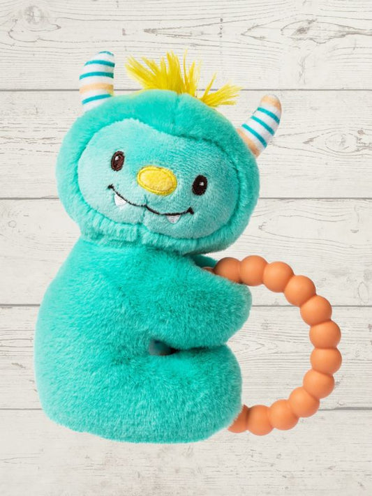 Teal plush toy with horns and a smile, holding an orange teething ring on a light wooden surface.