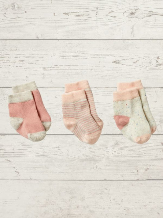 Three pairs of baby socks with pink and beige patterns on a light wooden surface.