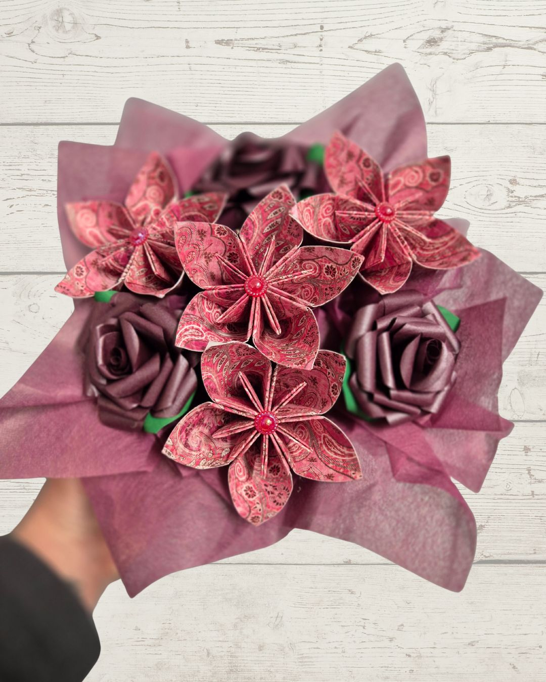 Bouquet of paper flowers wrapped in pink paper on a light wooden surface