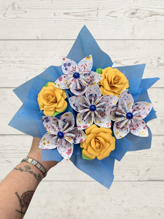 Bouquet of yellow paper roses and decorative butterflies on a wooden surface