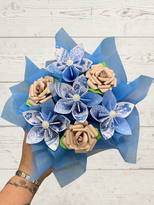 Bouquet of paper flowers with blue and beige roses on a wooden surface