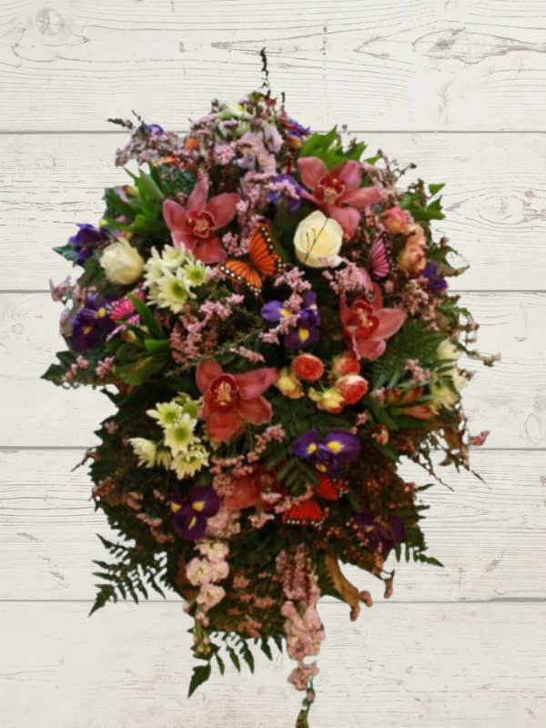 A custom-designed floral tribute arrangement featuring a variety of flowers including pink and purple orchids, carnations, and other foliage, intended to sit as the main flowers on a casket.