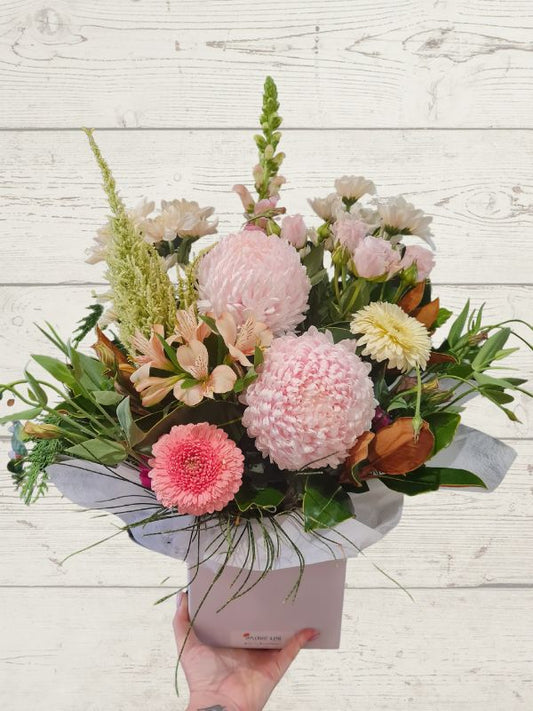 pastel flowers arranged into a container with pastel wrap.
