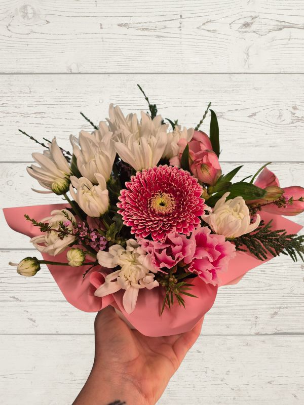 Bouquet of flowers held by a hand on a light wooden surface