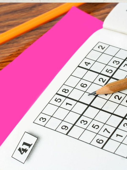 A puzzle book with a pen on top, featuring a grid of numbers and a pink eraser behind it.