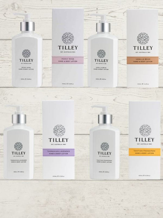 A collection of Tilley branded room spray bottles displayed against a wooden background. The bottles are varied in size and design, with a consistent white and silver label design featuring the Tilley logo.