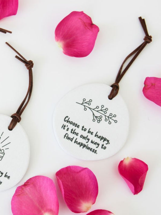 A white ceramic plaque with a quote about choosing happiness, embossed on it, and rope for hanging.