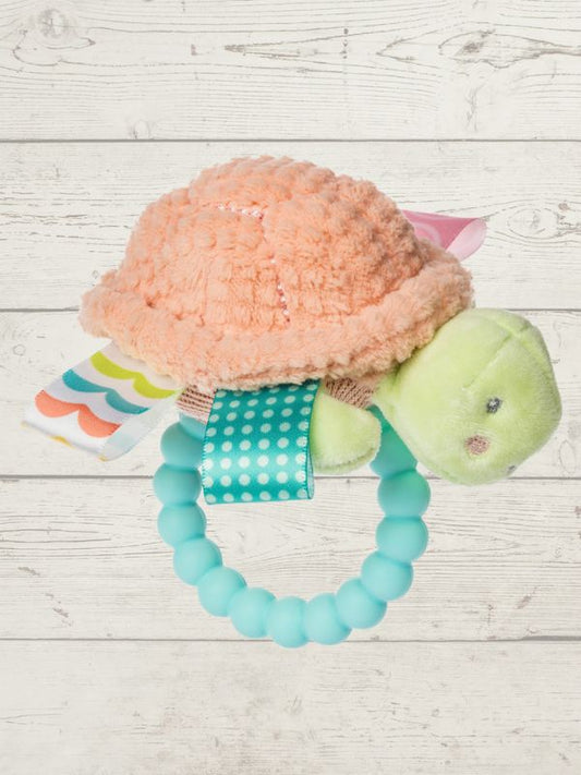 Turtle-shaped teething toy with a soft peach shell and green body on a light wooden surface.
