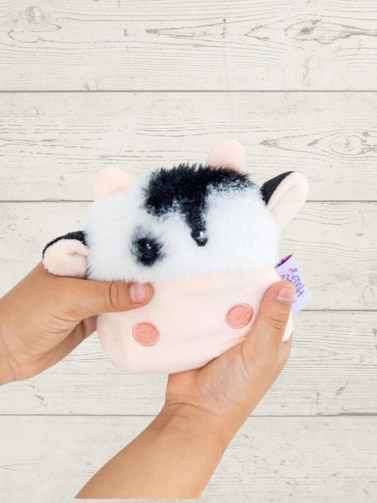 Plush toy resembling a black and white animal held by a hand on a light wooden surface
