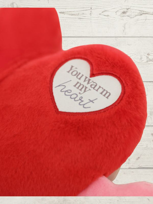 Red heart-shaped pillow with a white heart inside on a wooden surface