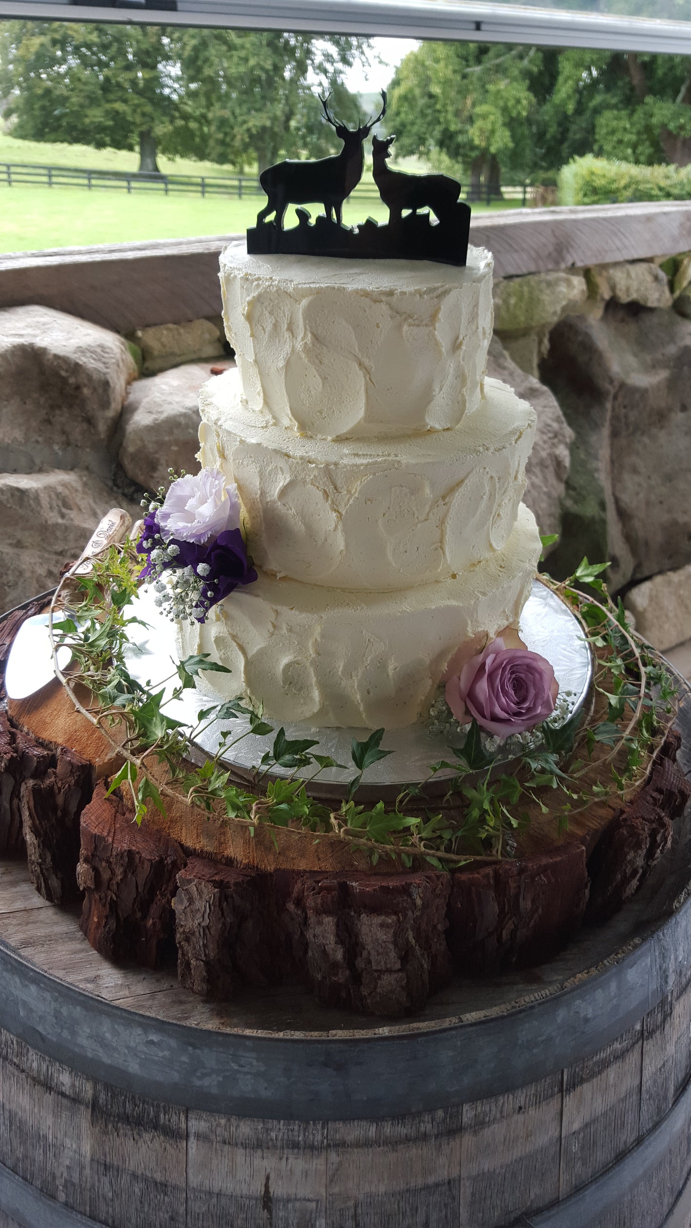 White cake with purple flower on a decorative stand outdoors