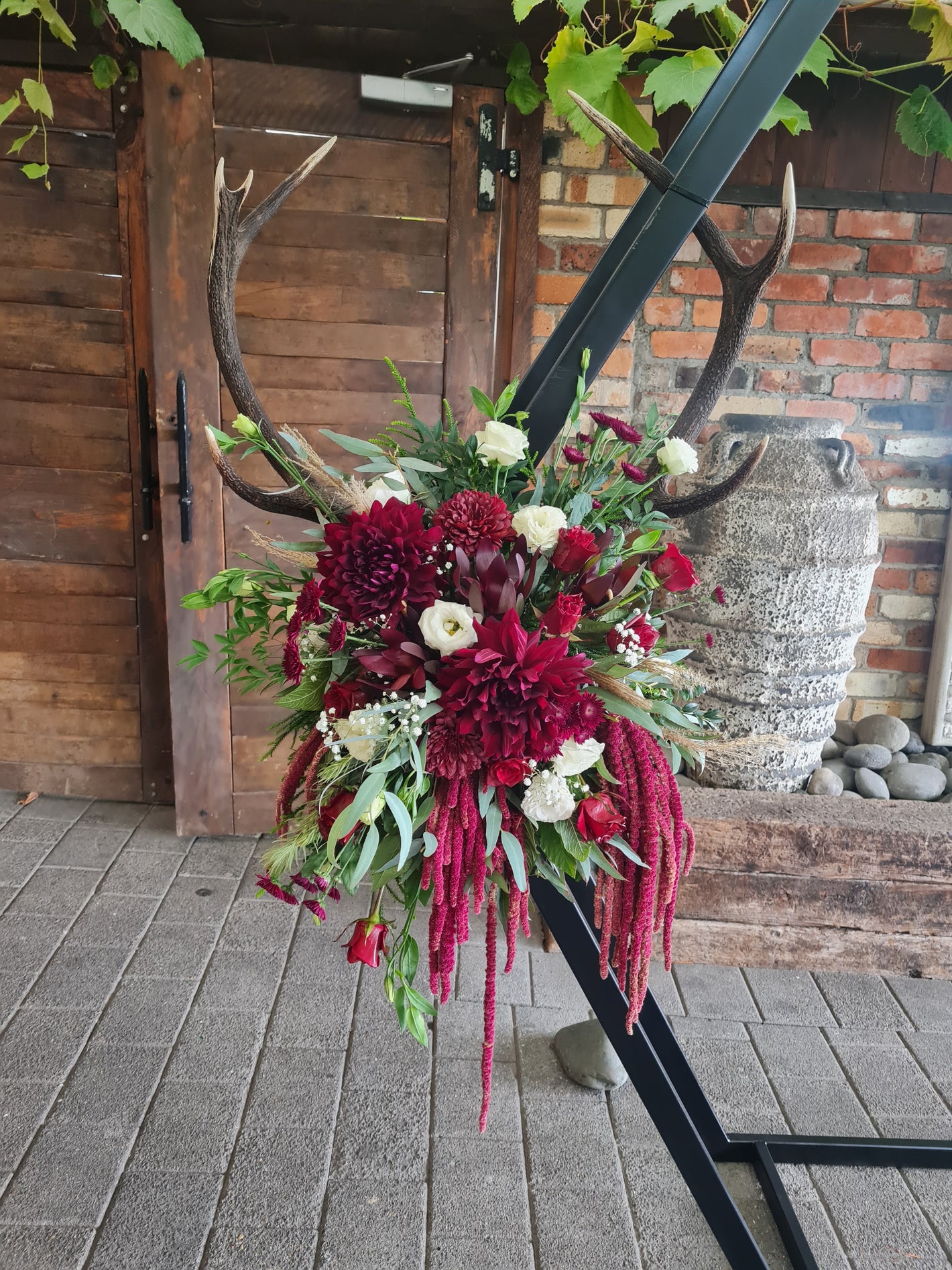 Floral arrangement with red and white flowers on a wooden door with antlers.