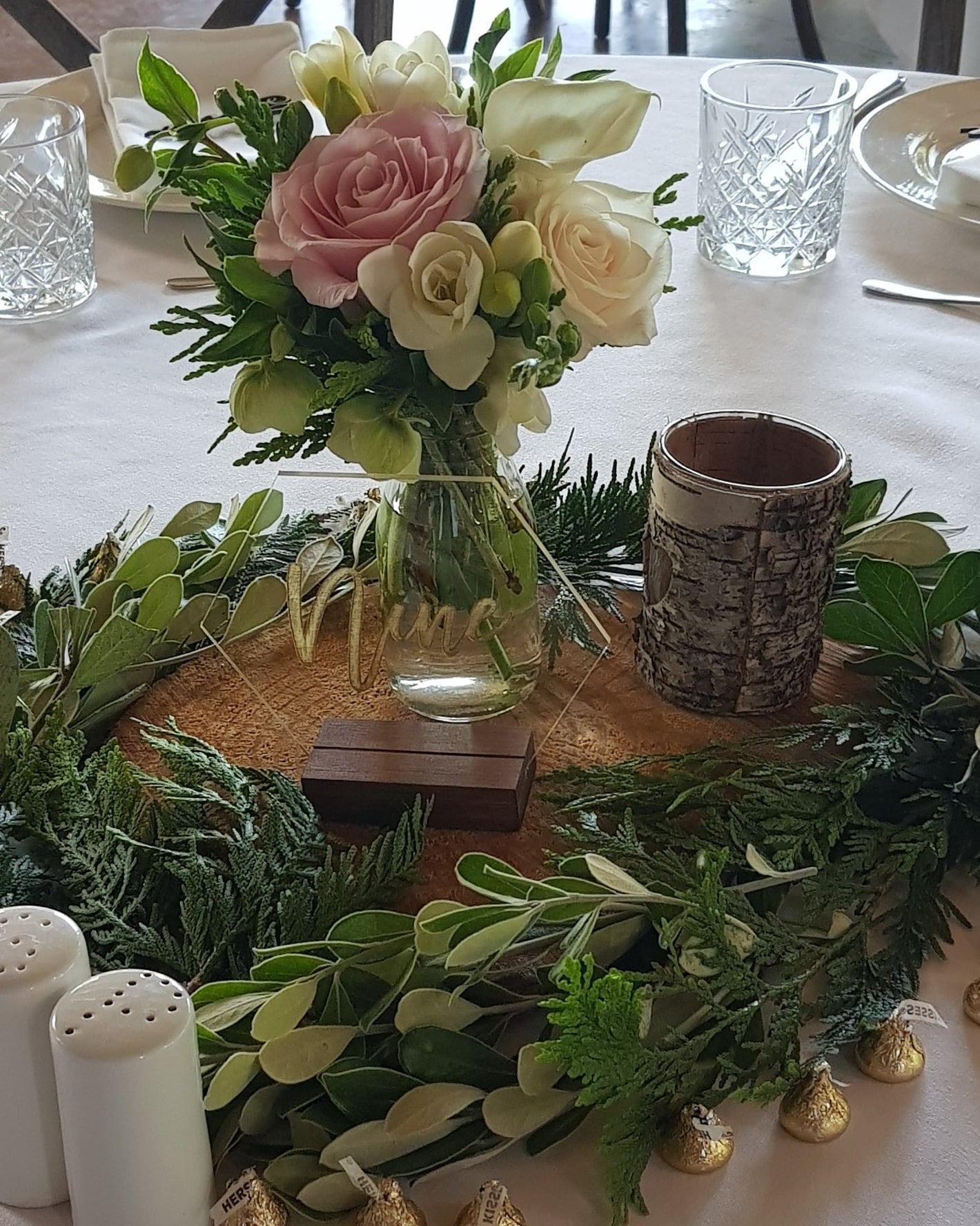 Decorative table setting with flowers, candles, and greenery on a white tablecloth.