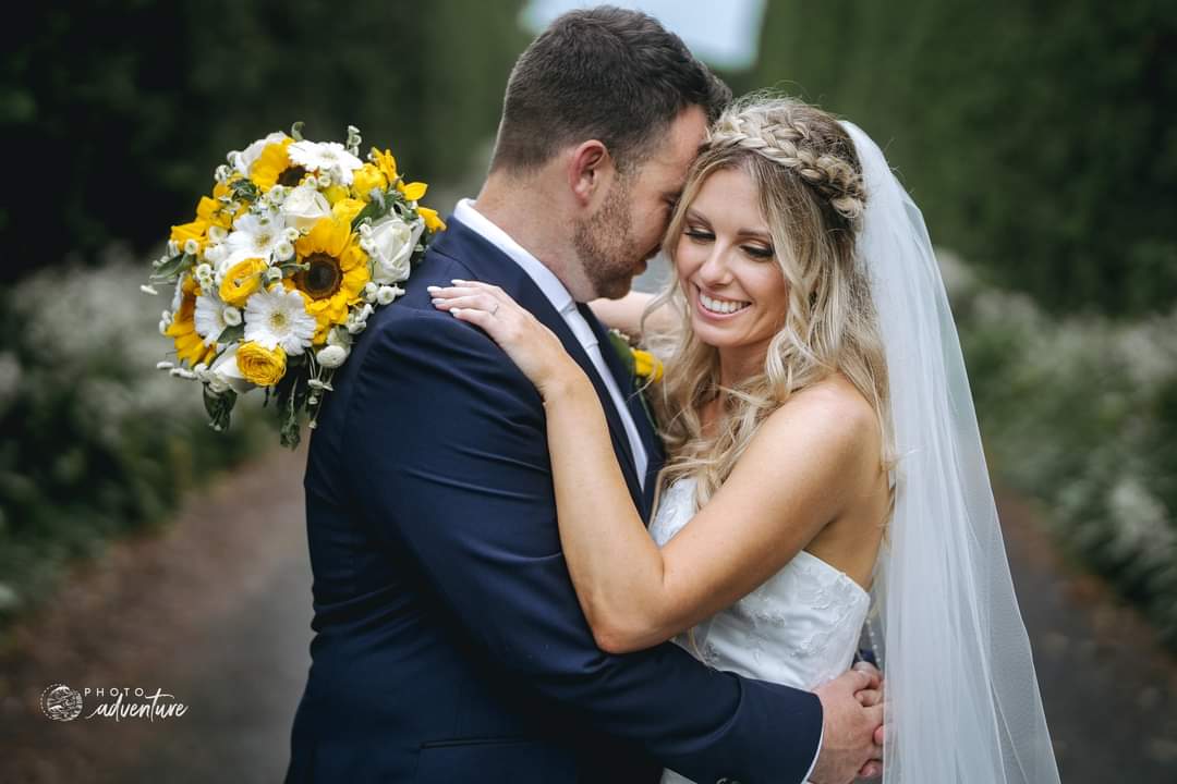 Wedding couple embracing with a bouquet of flowers with sunflowers, white gerbers, white roses and yellow roses
