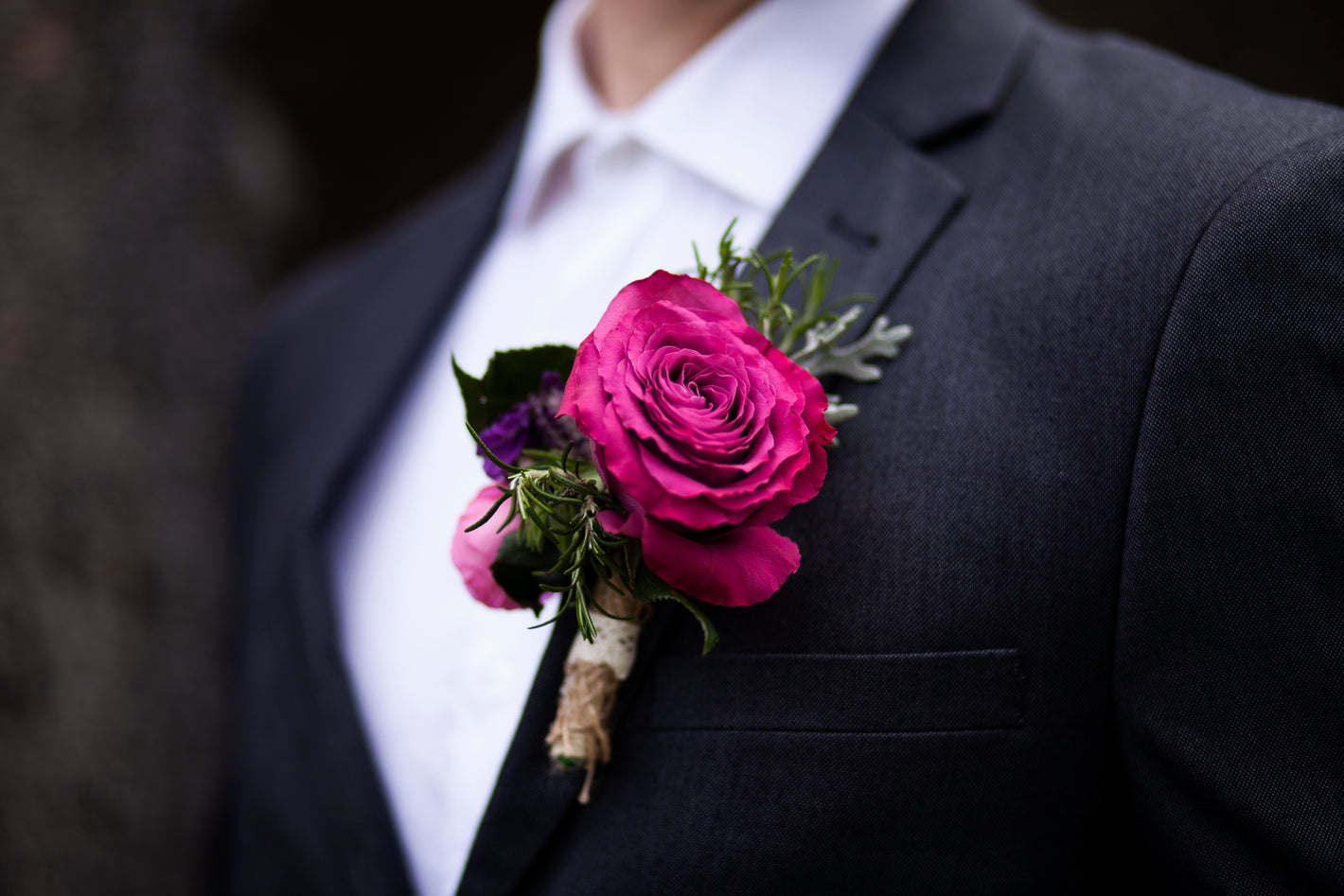 Close-up of a dark suit with a pink rose boutonniere against a blurred background