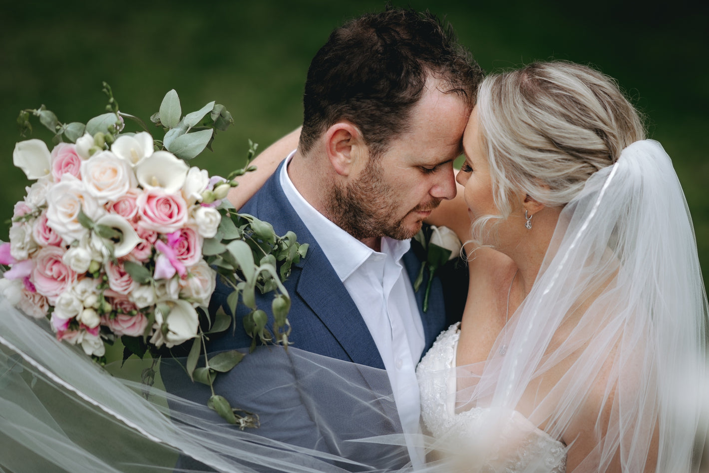 Wedding couple embracing with a bouquet of flowers in the foreground.