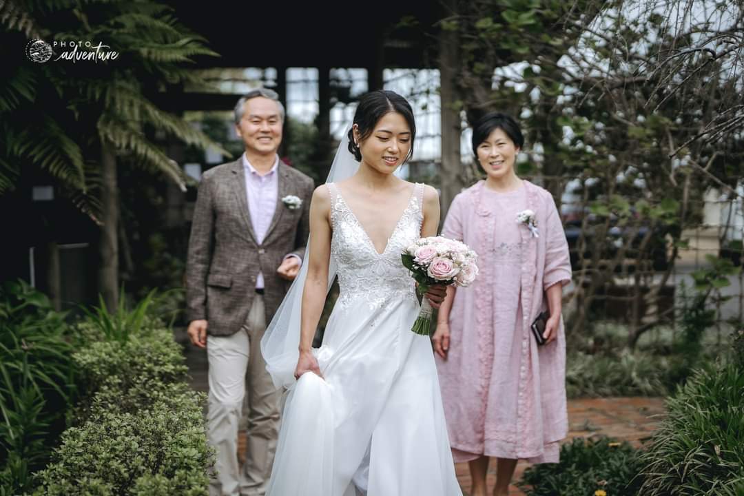 Woman in a wedding dress holding fresh posy of flowers with pink and white roses walking with two adults outdoors