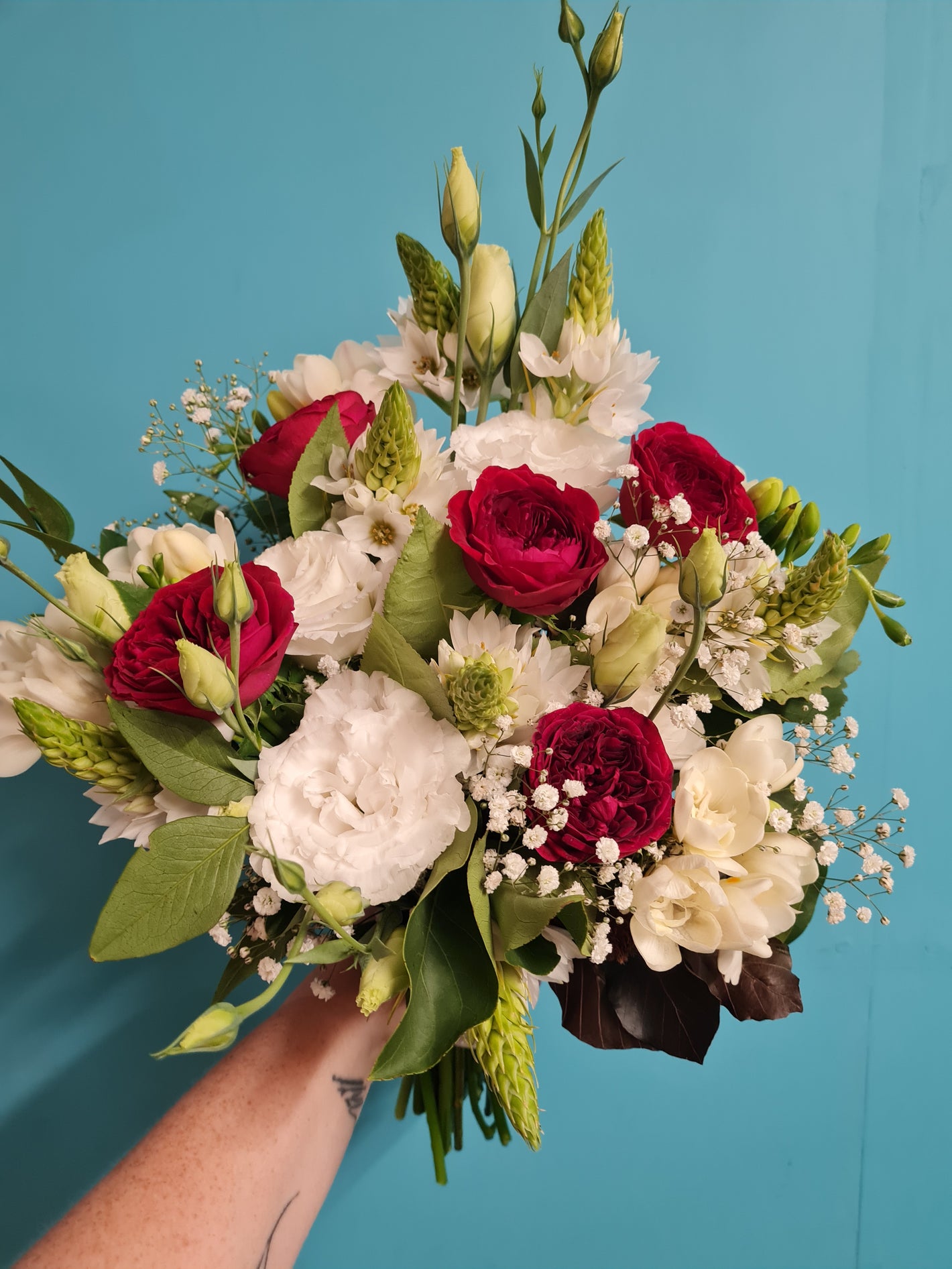 Bouquet of red, white, and green flowers held against a blue background
