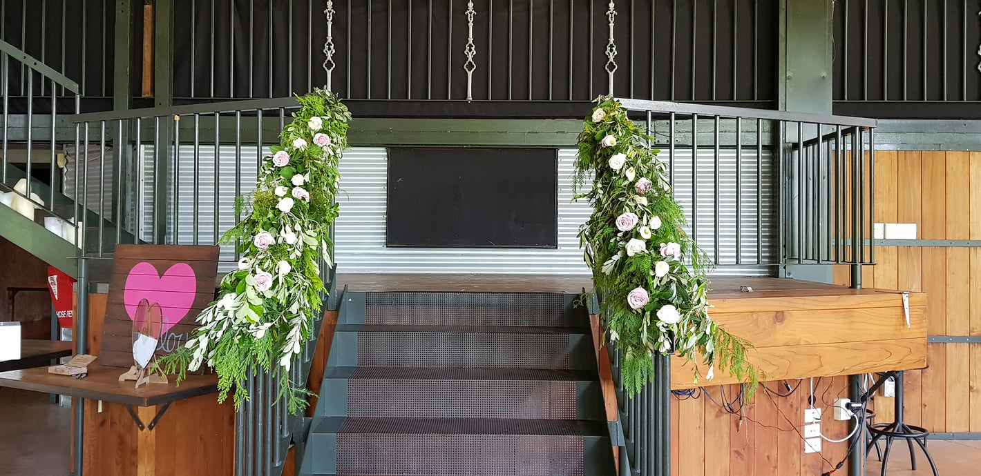Decorative floral arrangements hanging from a railing on stairway in an indoor setting.