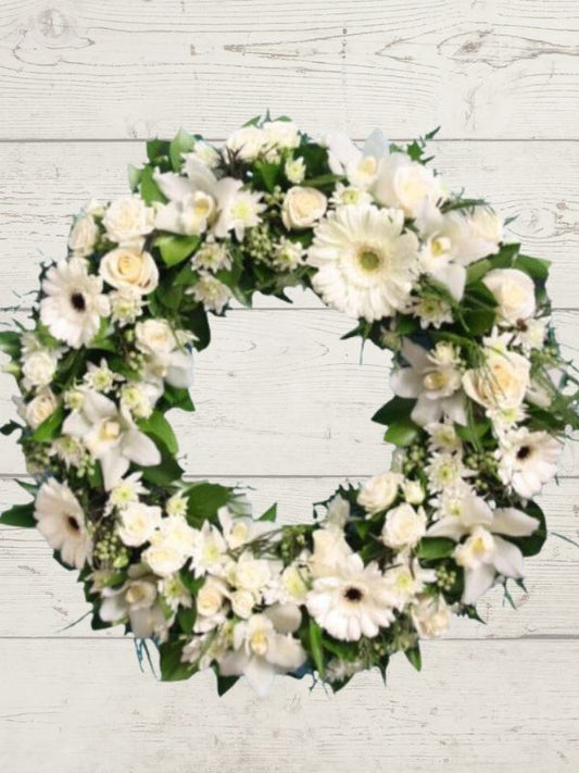 A formal white and green floral sympathy wreath displayed on a wooden background.