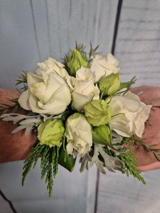 A wrist corsage featuring white and green flowers with leaves, attached to a white organza ribbon.