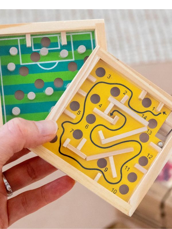 Wooden maze puzzle with a hand holding it, showing a soccer field design on one side.